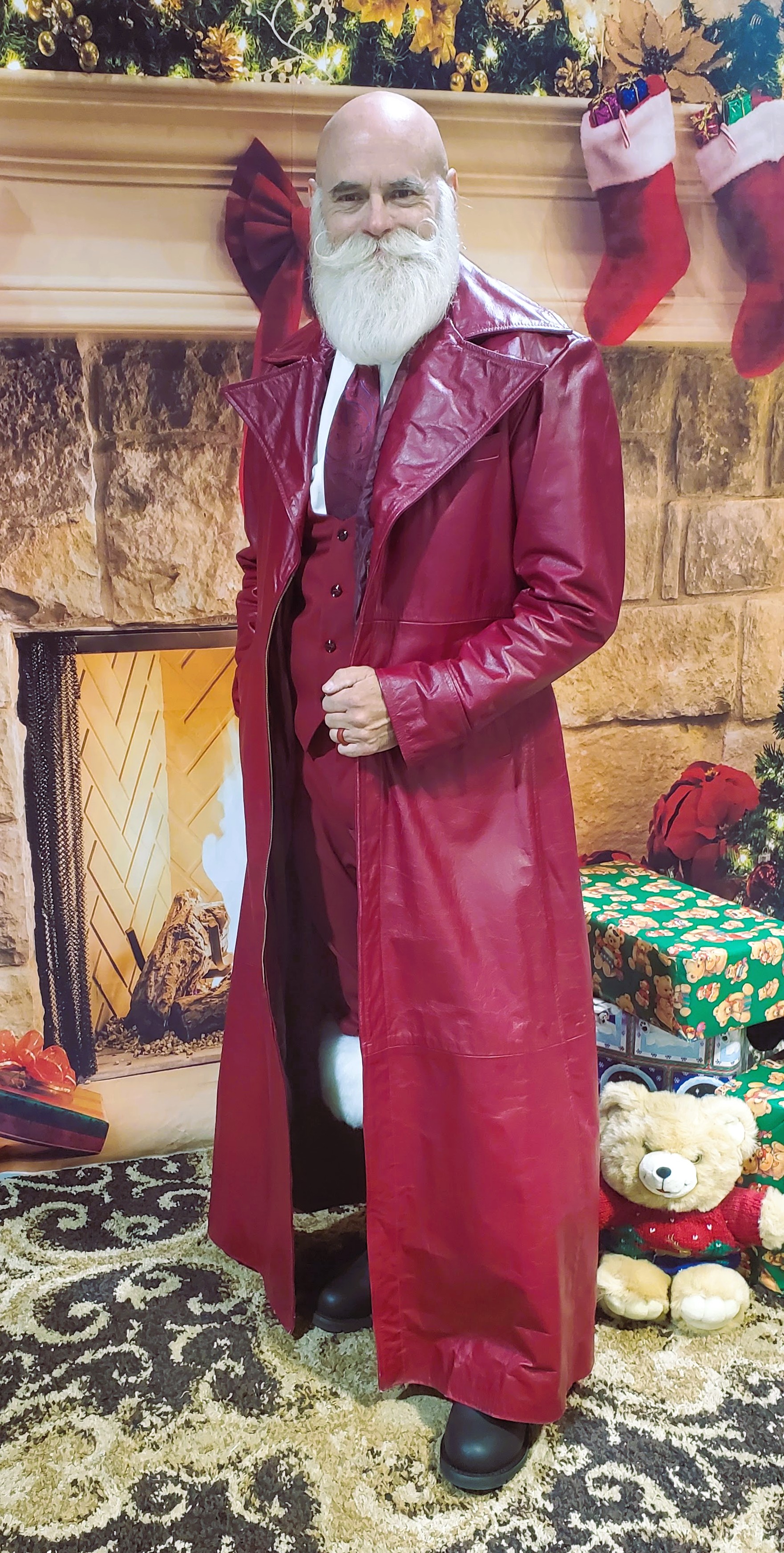 Santa in a long red leather coat beside a Christmas fireplace