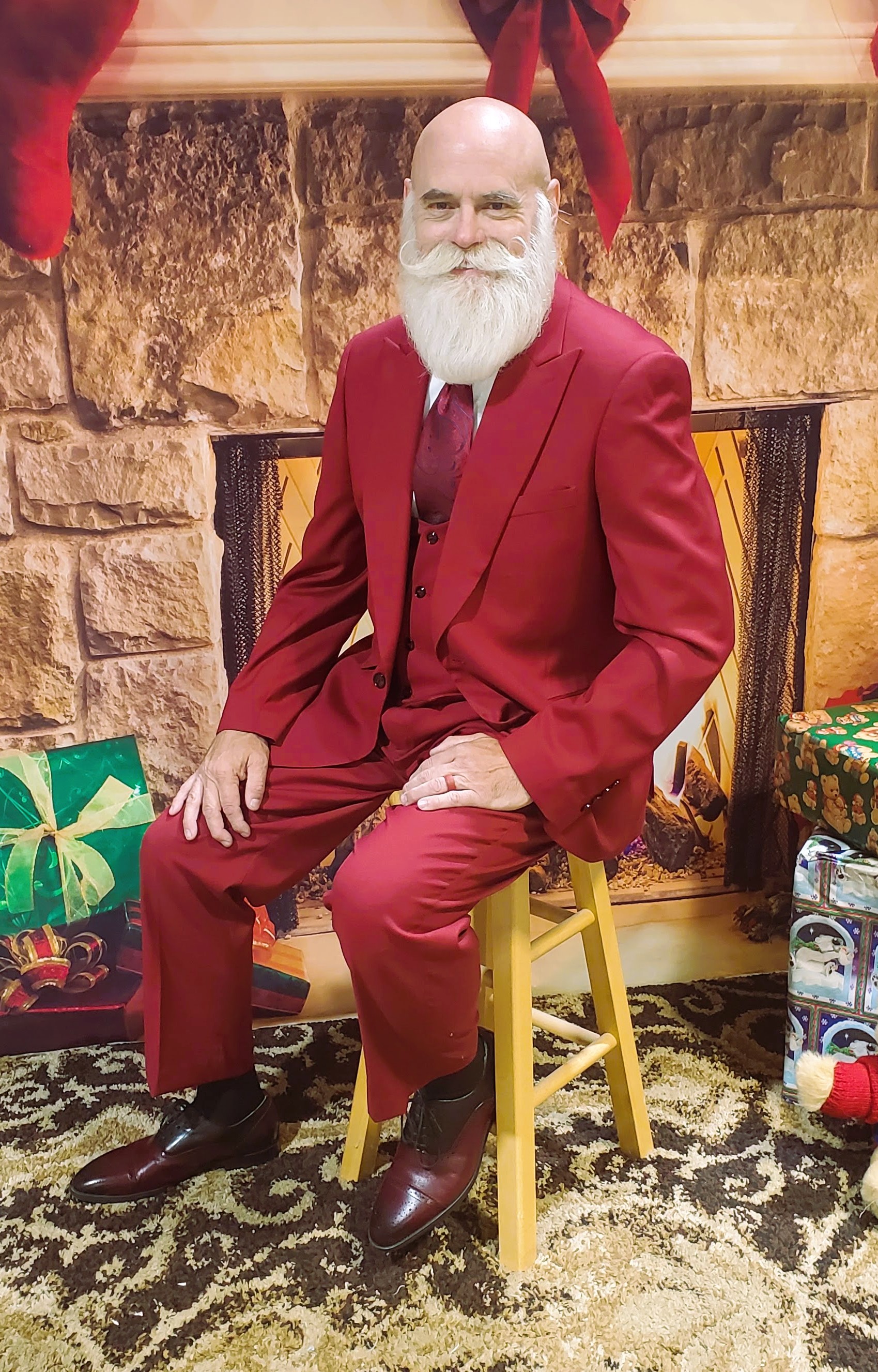 Santa seated in a tailored red suit beside a fireplace